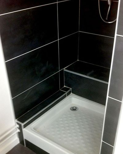 Douche avec receveur blanc et carrelage noir à la place de la baignoire