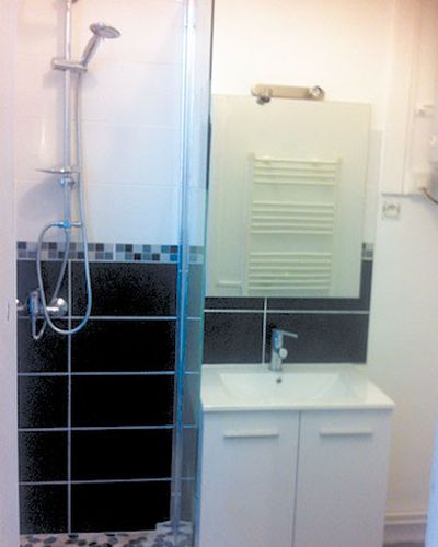 Douche carrelée de noir avec frise de mosaïque, meuble vasque blanc à côté