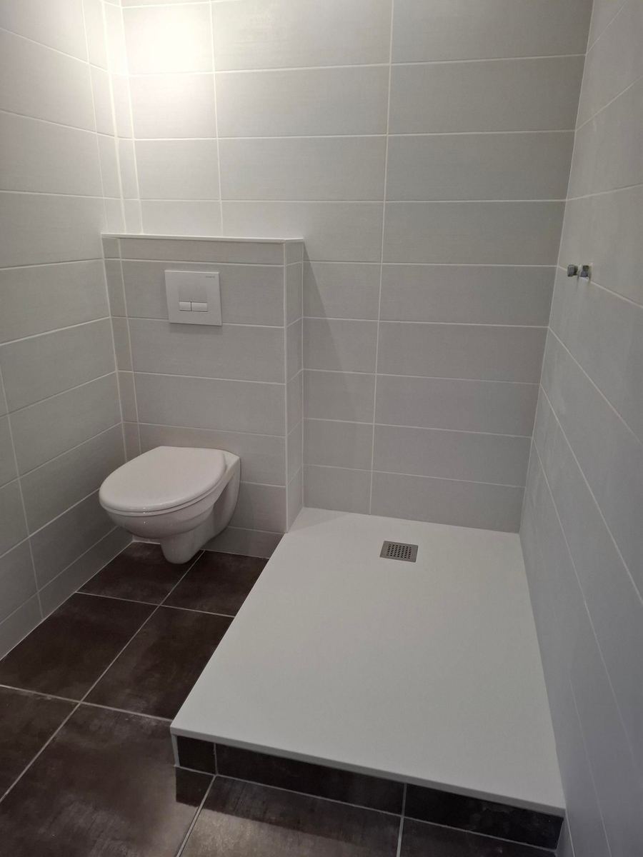 Salle d'eau terminée : carrelage gris, WC suspendu et receveur de douche blanc